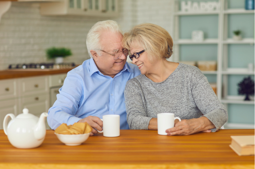 Smiling older couple sitting close together at their kitchen table with coffee