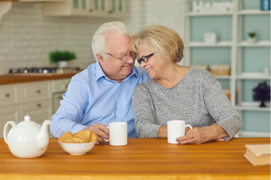Smiling older couple sitting close together at their kitchen table with coffee